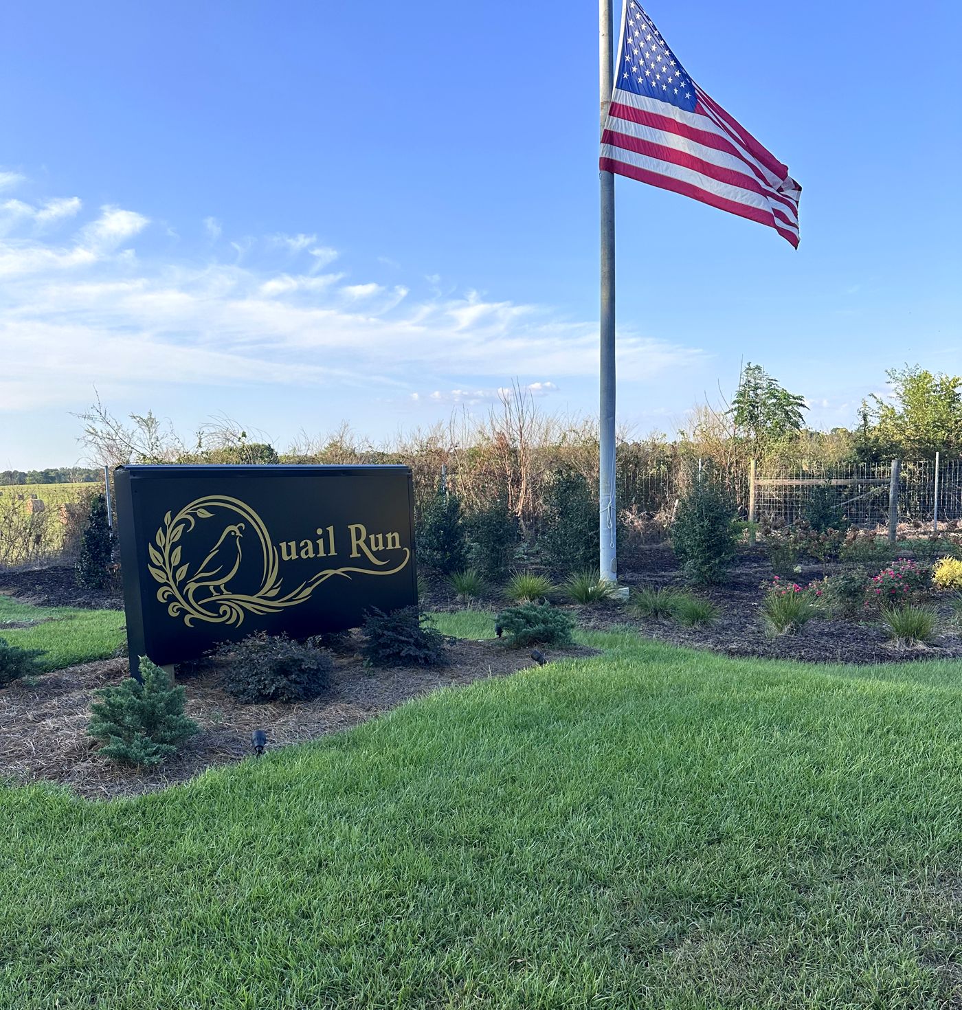 The Quail Run sign in the entrance landscaping, with the flag flying behind it