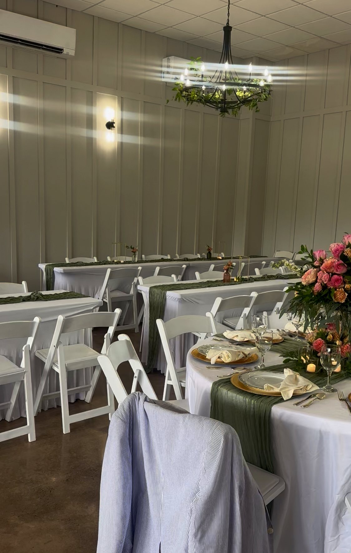 The main room set for a reception with white linens, sage runners and florals
